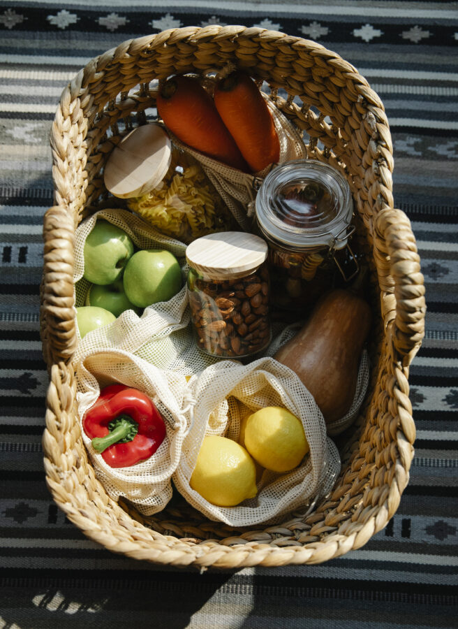 Wicker basket with vegetables and products placed on table in sunny day